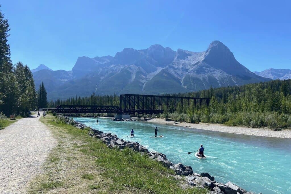 People paddle boarding on the bow river under canmore engine bridge on a beautiful summer day
