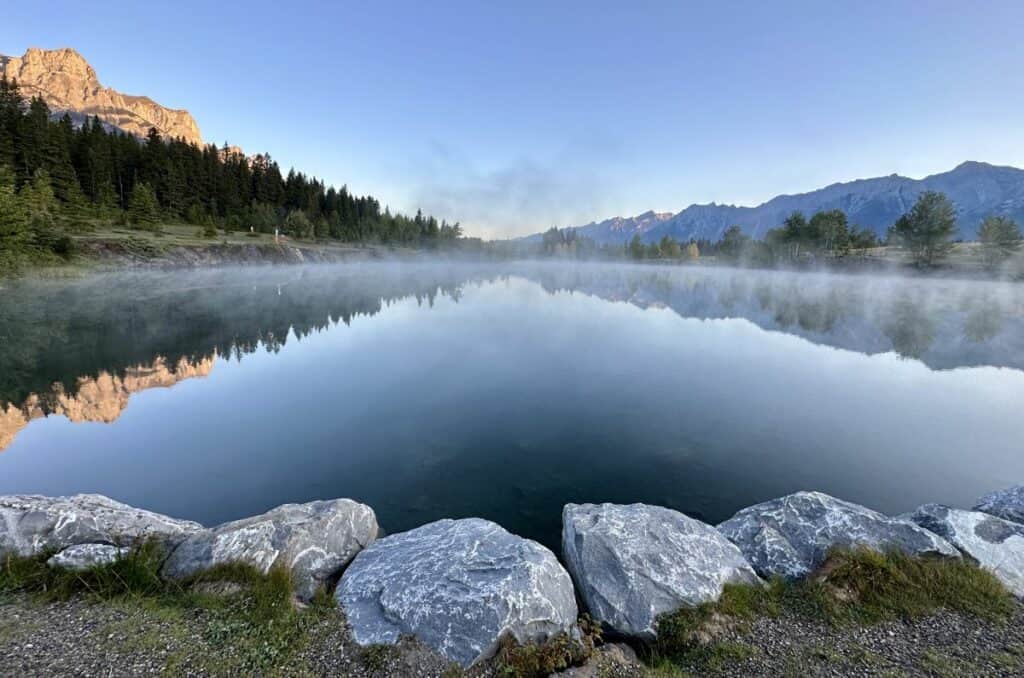 A mist hangs over quarry lake canmore alberta early in the morning as the sun rises
