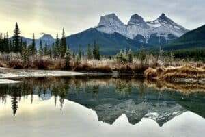 Three sisters viewpoint canmore reflected in a small pond in the early morning light
