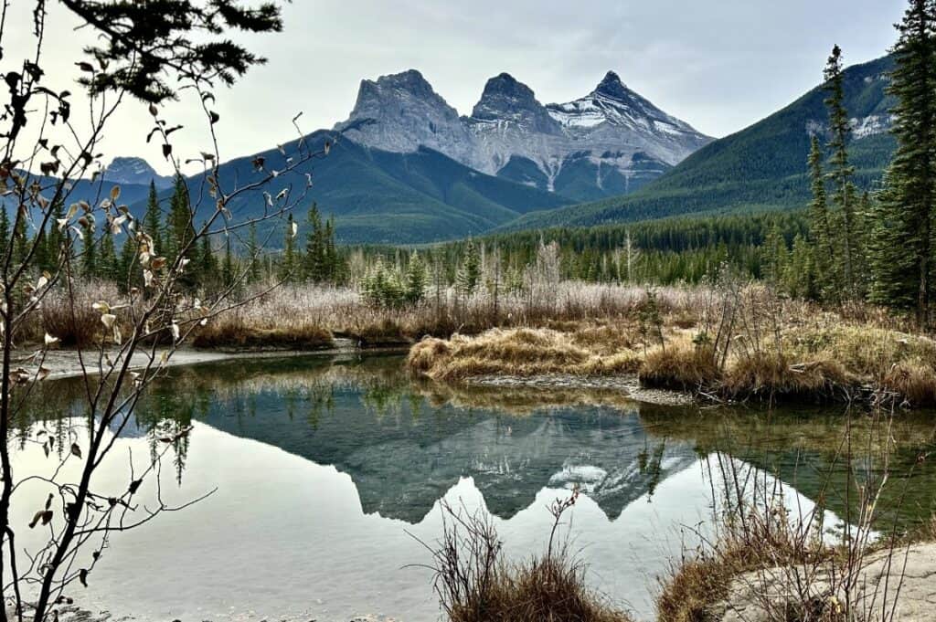 The three sisters mountains reflected in a still pond from the the three sisters viewpoint canmore alberta