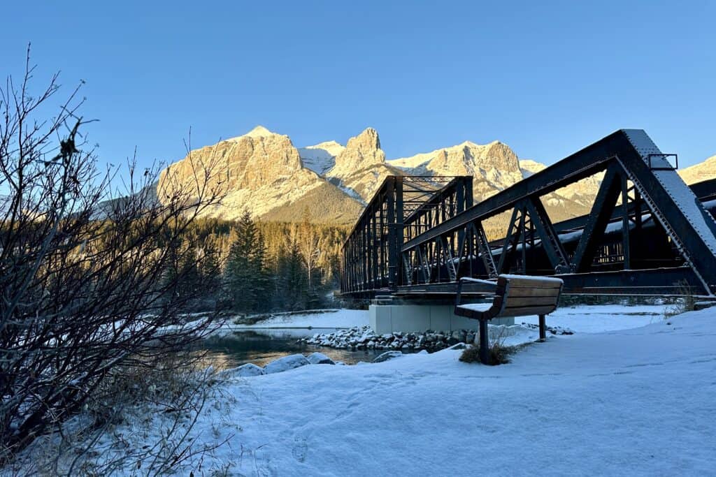 A bench stands in front of canmore engine bridge in winter at sunrise