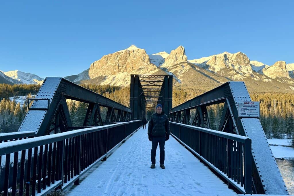 A man stands on canmore engine bridge in winter at sunrise with east end rundle in the background