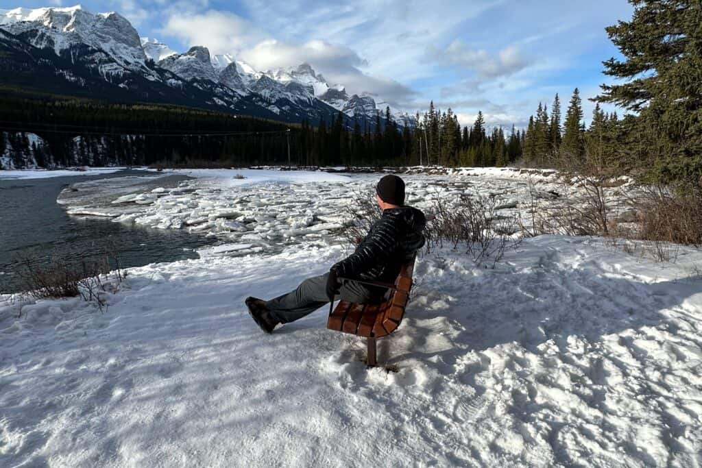A man sits on a bench by the bow river living in canmore alberta